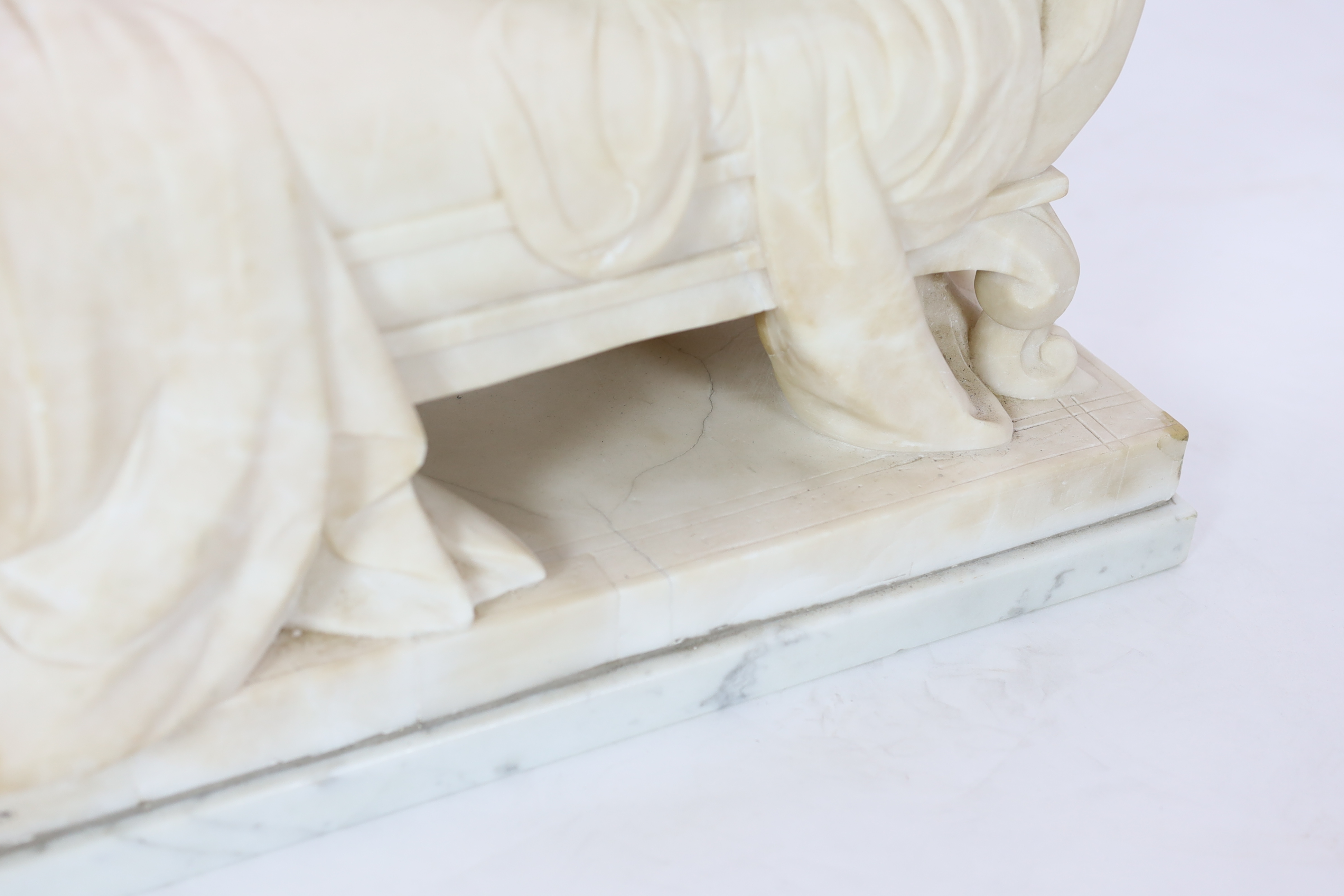 An early 20th century French carved white marble figure of a semi-clad woman seated upon a daybed, 50cm wide, 29cm deep, 52cm high